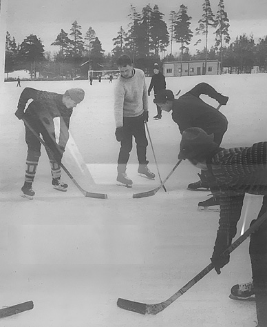 Koulun liikuntatunnilla: Aloituksessa oikealla Ilpo Niemi, vasemmalla Kari Kivelä ja etuoikealla Heikki Haapiainen. Kiekkoa pudottamassa opettaja Pasi Jaakkola, joka oli huippupesäpalloilija - Itä-Länsi-pelaaja. Pelaajat ovat urheilukentän jäällä, vielä ei kaukaloa näy taustalla. Kuva: Kari Kivelä.